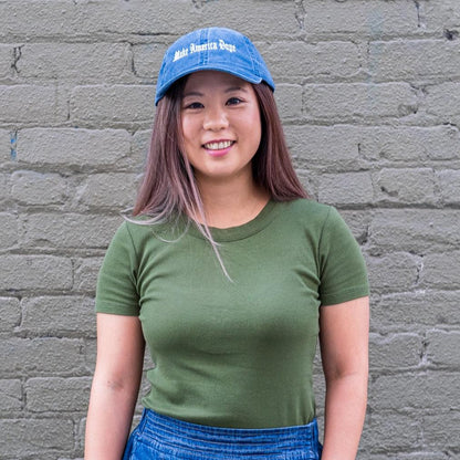 Woman standing in front of olive wall wearing blue Make America Dope hat
